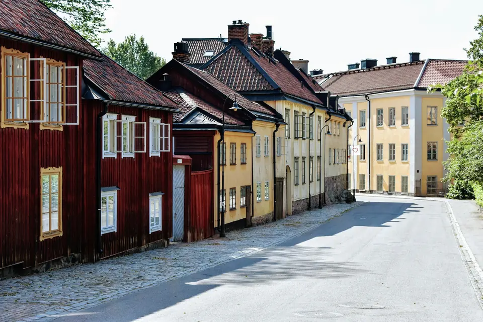 Gate med røde og gule trehus og en lys murgård i sommersol