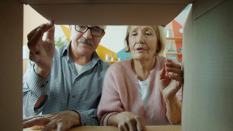 Eldre par som ser ned i en åpen pappeske, fotografert fra innsiden av esken